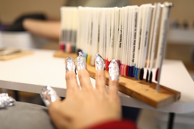 La mano de la mujer con papel de aluminio en las uñas está de pie junto a muestras de barniz con paleta de colores.