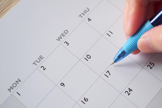 Mano de mujer con pluma escribiendo en el concepto de reunión de cita de planificación de negocios de fecha de calendario