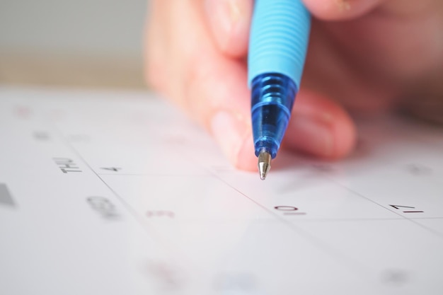 Mano de mujer con pluma escribiendo en el concepto de reunión de cita de planificación de negocios de fecha de calendario