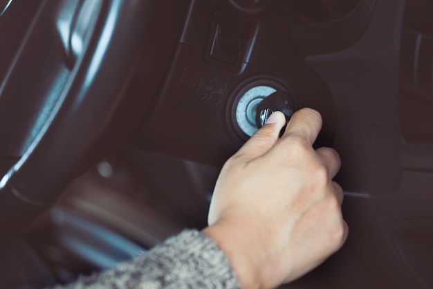 La mano de la mujer pone la llave en el encendido y enciende el motor del automóvil en tono de color vintage