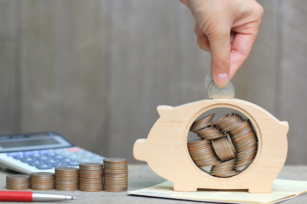 Mano de mujer poniendo una moneda en madera hucha