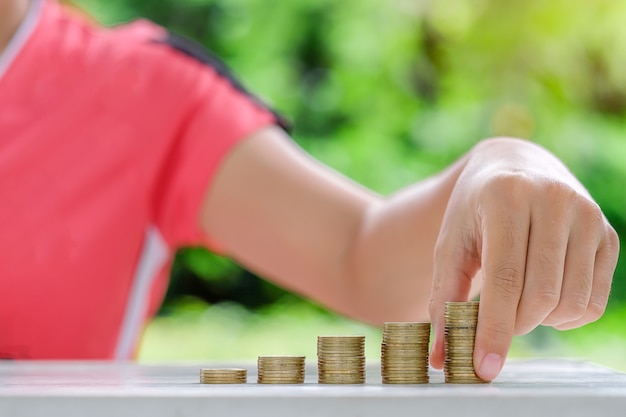 Mano de mujer poniendo monedas, monedas de oro pila en mesa de madera