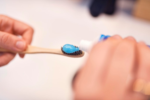 Mano de mujer poniendo pasta de dientes en un cepillo de dientes de bambú higiene dental cepillarse los dientes con pasta de dientes granulada