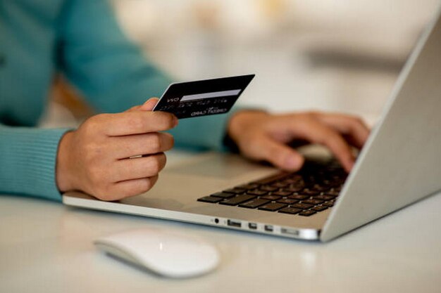 Mano de mujer en primer plano usando tarjeta de crédito y portátil para comprar en línea