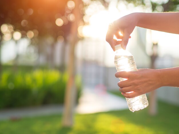 Mano de la mujer del primer que sostiene la botella de agua potable durante puesta del sol.