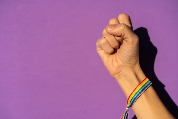 Foto mano de una mujer con el puño cerrado con fuerza sobre el símbolo de lucha a favor del feminismo fondo morado luchando a favor de las mujeres fuerza femenina bandera lgtb