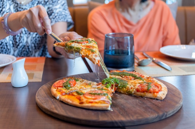 Mano de la mujer que escoge un pedazo de pizza en el tablero de madera en restaurante.