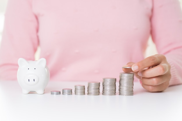 Mano de la mujer que pone la moneda del dinero en la pila de monedas. Concepto de ahorro de dinero.