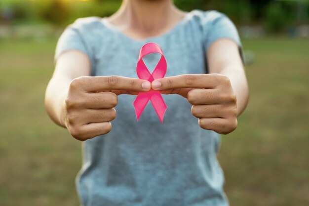 Mano de la mujer que sostiene conciencia rosada del cáncer de pecho de la cinta. concepto de salud