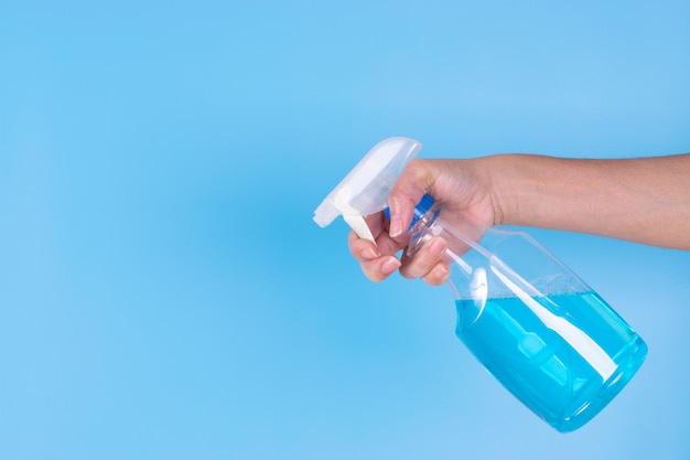 La mano de la mujer que sostiene el espray de alcohol en fondo del cielo azul. Pulverizar desinfectante para evitar Covid-19.