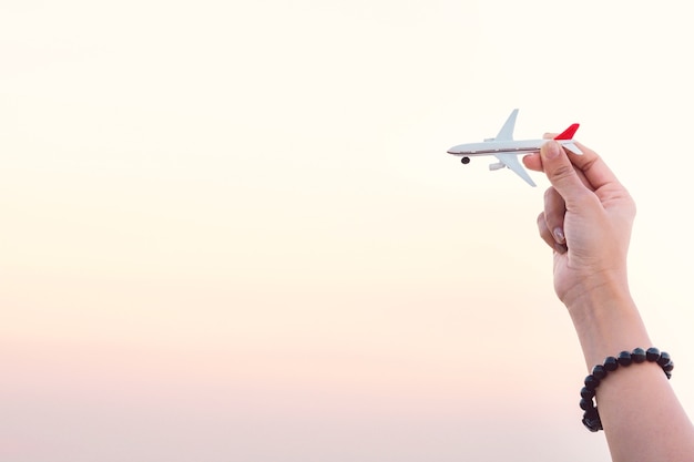 Mano de la mujer que sostiene el modelo del aeroplano en fondo del mar del cielo del atardecer y del verano.