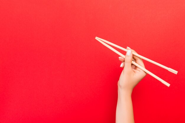 La mano de la mujer que sostiene los palillos en fondo rojo. Concepto de comida china con espacio vacío para su diseño