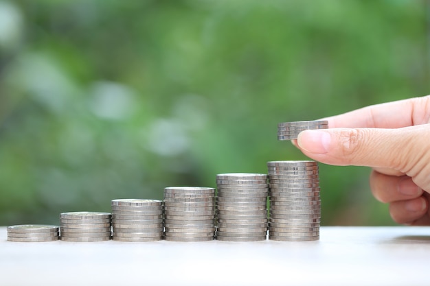 Mano de mujer que sostiene la planta que crece en la pila de monedas dinero y gráfico sobre fondo verde natural