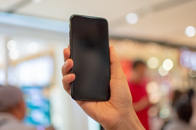 La mano de la mujer que sostiene el teléfono elegante con el fondo de la falta de definición.