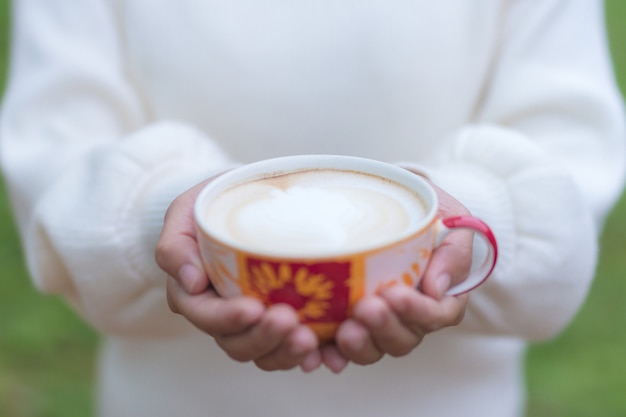 Foto mano de la mujer que sostiene un vidrio de café en el jardín.