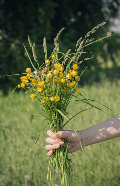 La mano de una mujer con un ramo de flores silvestres en un fondo forestal