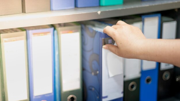 Foto la mano de la mujer recoge una carpeta del documento en la fila de carpetas de archivos que están en los estantes