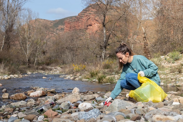 Mano de mujer recogiendo basura para limpiar en el río con vista natural de otoño