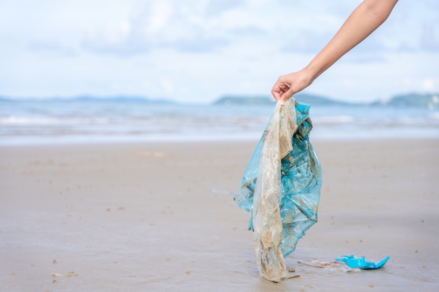 Foto mano de mujer recogiendo una bolsa de plástico usada en la playa de arena