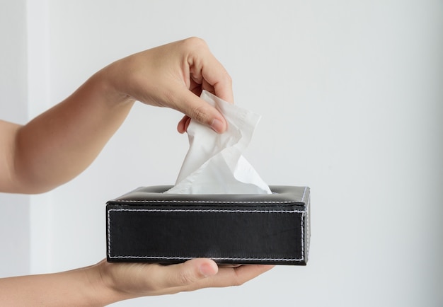 Mano de mujer recogiendo papel de seda blanco de caja de pañuelos.