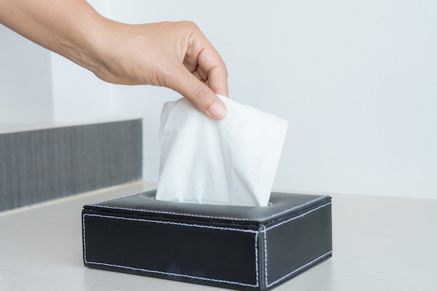 Mano de mujer recogiendo papel de seda blanco de caja de pañuelos.