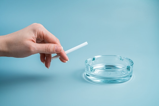 La mano de una mujer rompe un cigarrillo sobre un fondo azul claro. Vista lateral con espacio de copia.