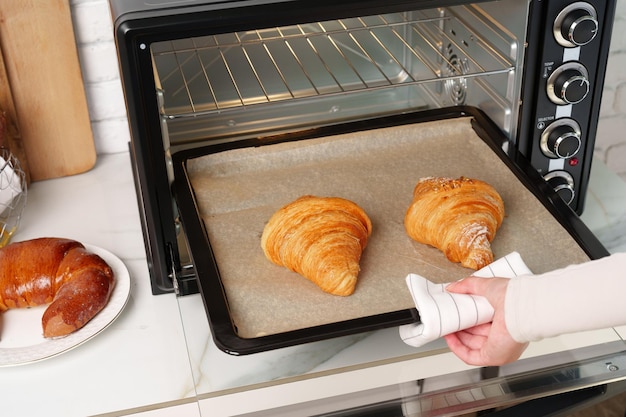 Foto la mano de la mujer sacando deliciosos croissants del horno eléctrico en la cocina