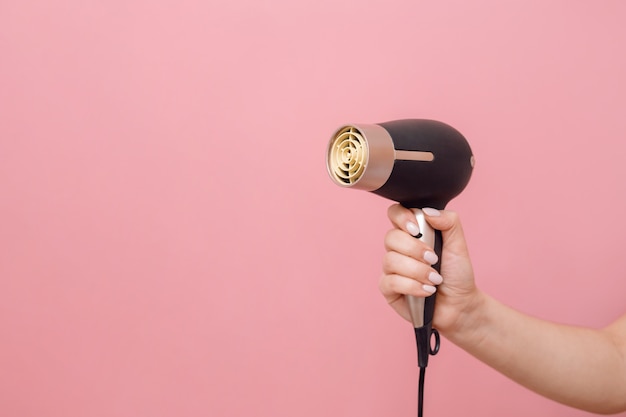 en mano de mujer secador de pelo en pared rosa