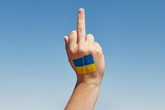 La mano de la mujer con el símbolo de la bandera ucraniana muestra el signo de mierda contra el cielo azul Detener la guerra