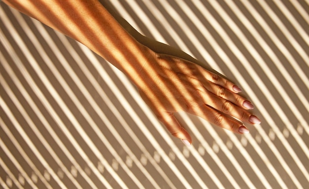 La mano de una mujer con sombras proyectadas desde las persianas.