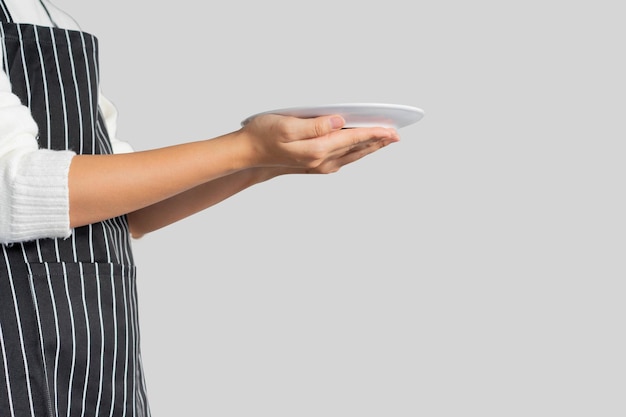 Foto mano de mujer sostenga el plato vacío agregue su contenido en la imagen aislada en fondo gris