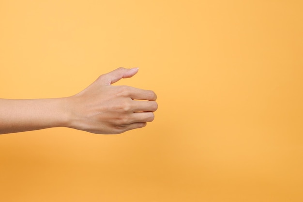 La mano de la mujer sosteniendo algo como una botella o una lata aislada sobre un fondo amarillo