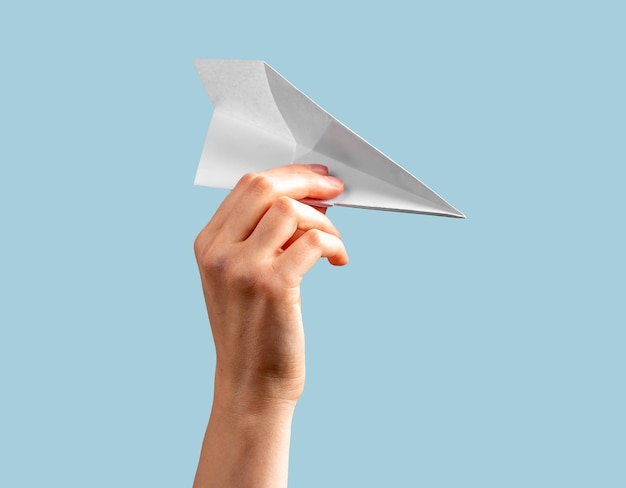 Foto mano de mujer sosteniendo avión de origami sobre fondo azul avión de papel volador