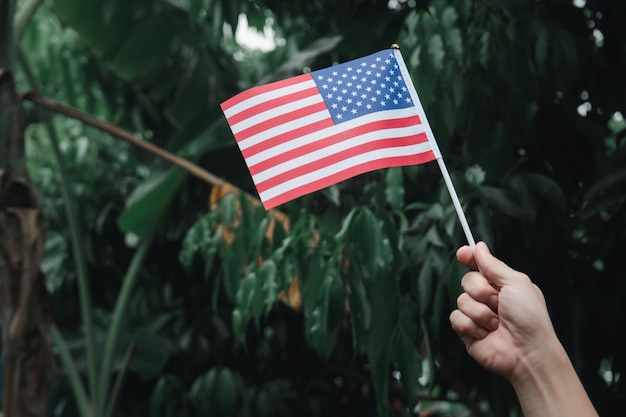 Mano de mujer sosteniendo la bandera de Estados Unidos en bosque verde. 4 de julio, día de la independencia americana