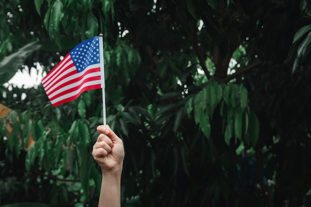 Mano de mujer sosteniendo la bandera de Estados Unidos en bosque verde