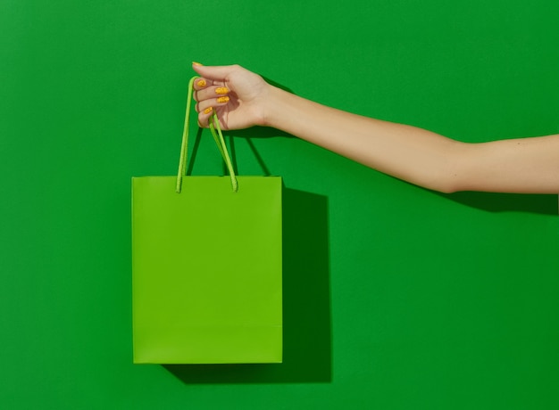 Mano de mujer sosteniendo la bolsa de compras sobre fondo verde