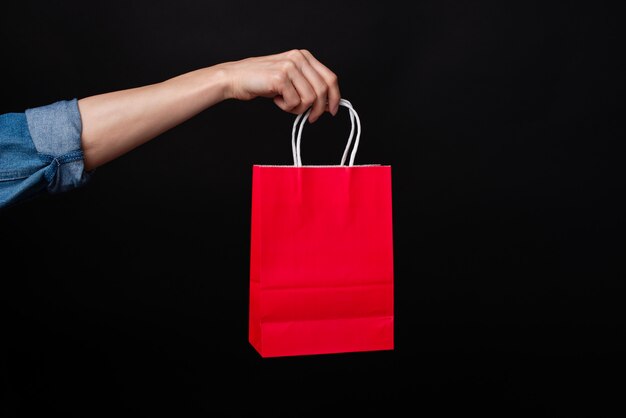 Mano de mujer sosteniendo bolsa roja sobre fondo negro