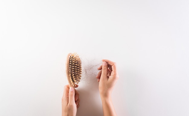 Mano de mujer sosteniendo la caída del cabello o caída del cabello en peine sobre fondo blanco.