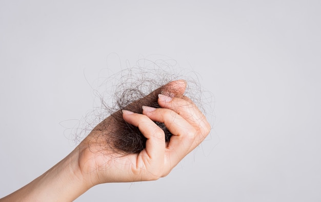 Mano de mujer sosteniendo la caída del cabello sobre fondo gris. Cuidado de la salud y médico, concepto de problema de pérdida de cabello.