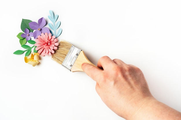 Mano de mujer sosteniendo un cepillo frente a las flores de papel