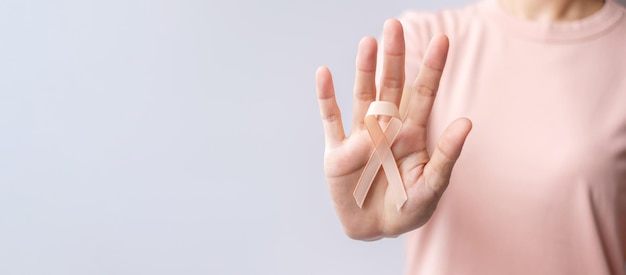 Foto mano de mujer sosteniendo la cinta de melocotón para el mes de concientización sobre el cáncer uterino de septiembre concepto de atención médica y día mundial del cáncer