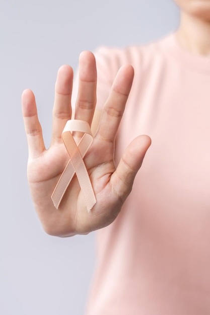 Foto mano de mujer sosteniendo la cinta de melocotón para el mes de concientización sobre el cáncer uterino de septiembre concepto de atención médica y día mundial del cáncer