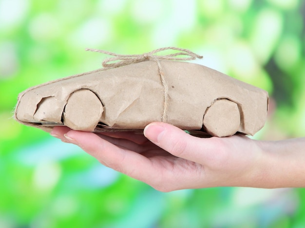 Foto mano de mujer sosteniendo un coche envuelto en papel kraft marrón sobre fondo de naturaleza