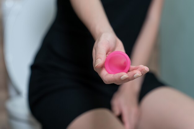 Mano de mujer sosteniendo la copa menstrual en el baño. Enfoque selectivo. Concepto de higiene.