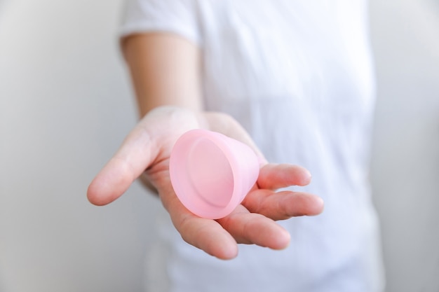 Mano de mujer sosteniendo la copa menstrual rosa aislada sobre fondo blanco. Higiene ginecológica ecológica alternativa moderna de mujer en período de menstruación. Recipiente para sangre en mano de niña.