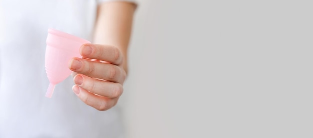 Mano de mujer sosteniendo copa menstrual rosa aislada sobre fondo blanco mujer alternativa moderna eco gyne