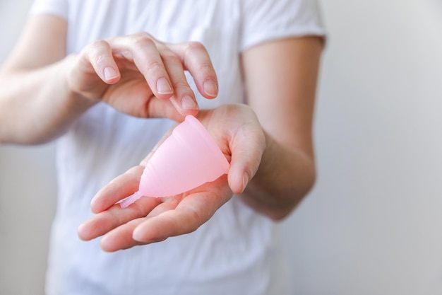 Mano de mujer sosteniendo copa menstrual rosa aislada sobre fondo blanco mujer moderna alternativa eco gyne ...