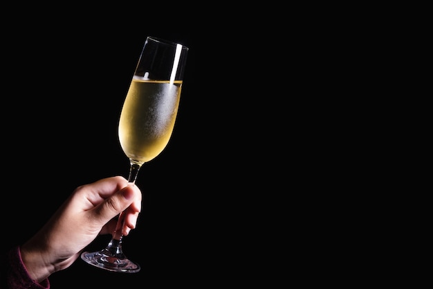 Mano de mujer sosteniendo copas de champagne en el fondo negro