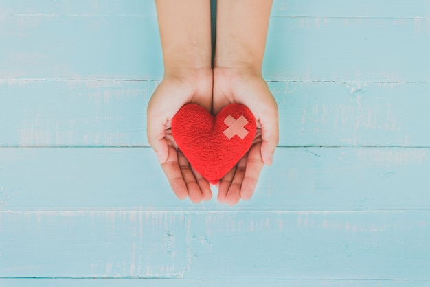 Foto mano de mujer sosteniendo corazón rojo sobre fondo azul de madera