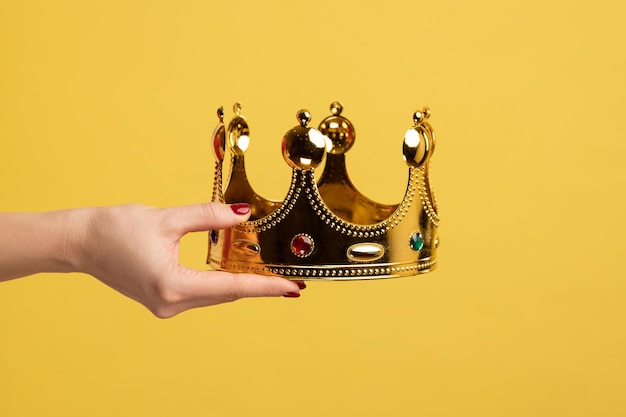 Foto mano de mujer sosteniendo la corona de oro concepto de ceremonia de entrega de premios estatus privilegiado posición superior